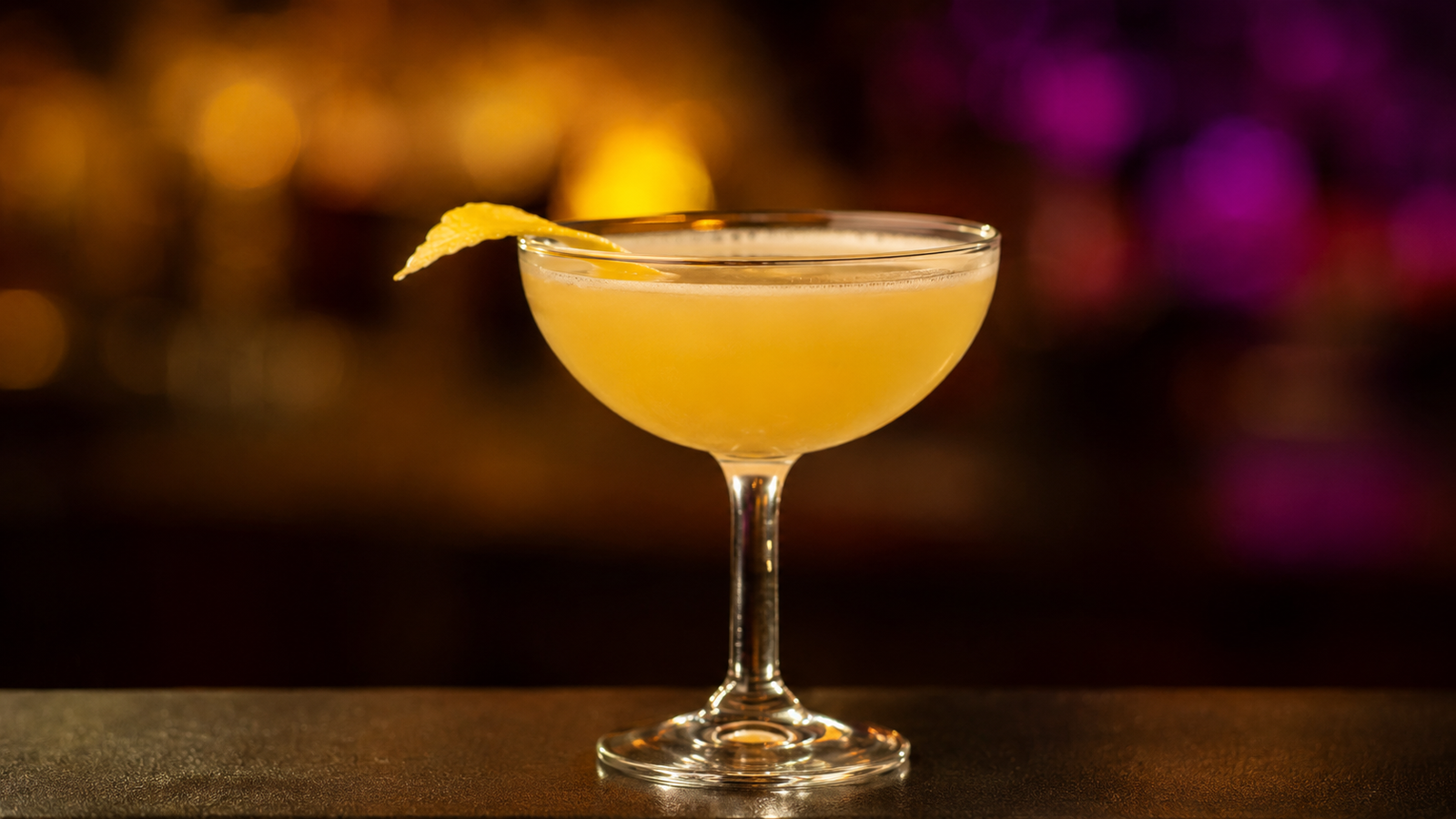 Bee’s Knees vor extrem unscharfem Neonhintergrund in der Farbe des Drinks